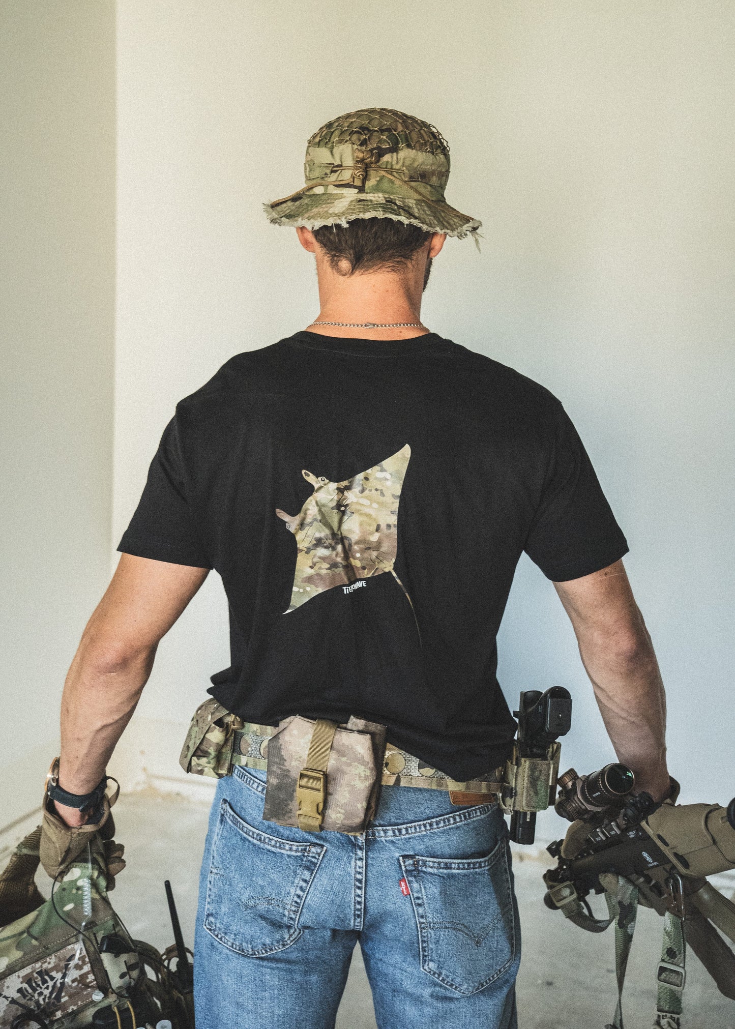 Person wearing a black t-shirt with a star design, blue jeans, and a camouflage hat, holding rifles.